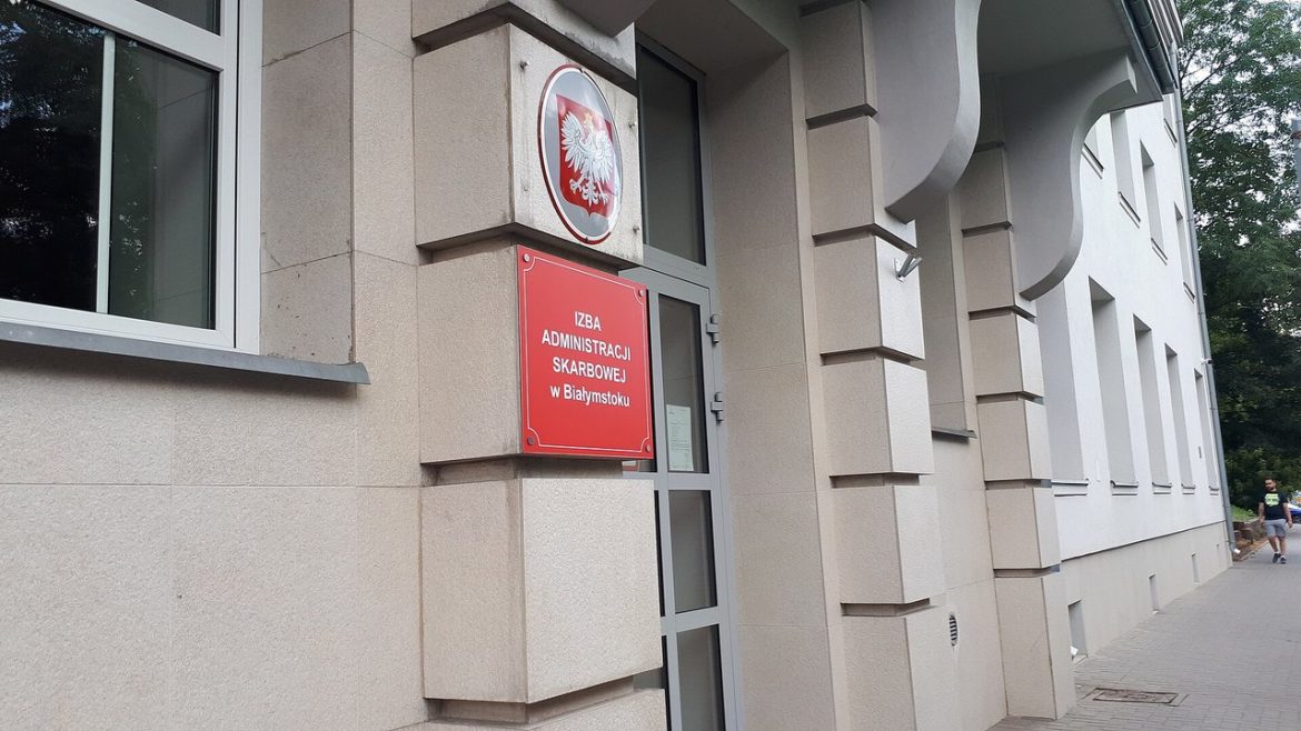 Wejście do Izby Administracji Skarbowej w Białymstoku z godłem i czerwoną tablicą urzędu